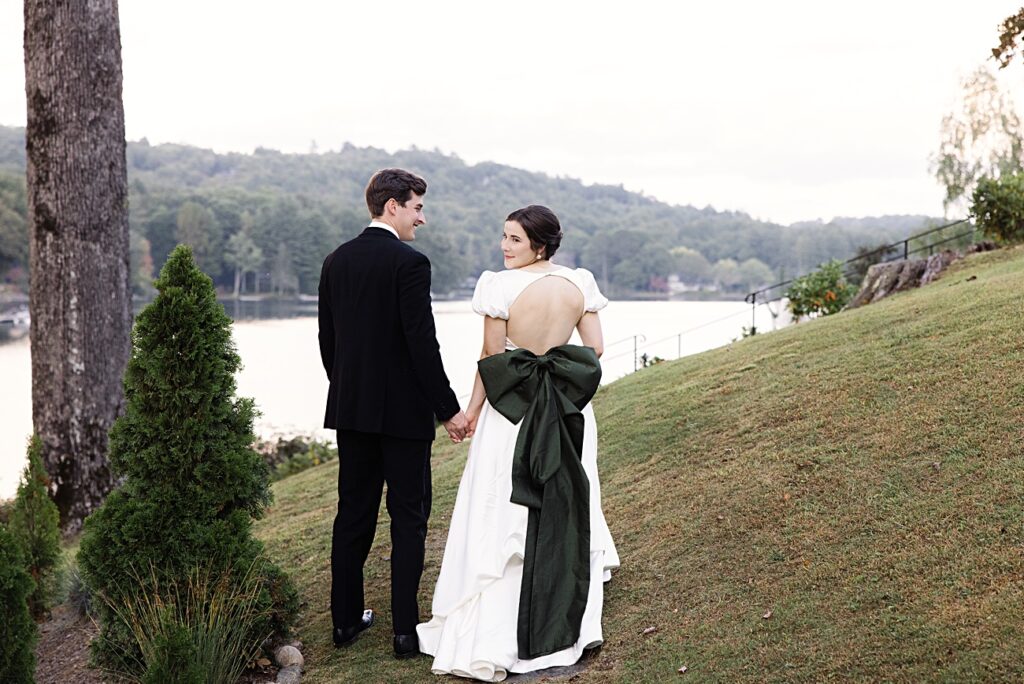 Bride with Structural Green Bow Gown Walking Toward Lake Toxaway at Greystone Inn Wedding